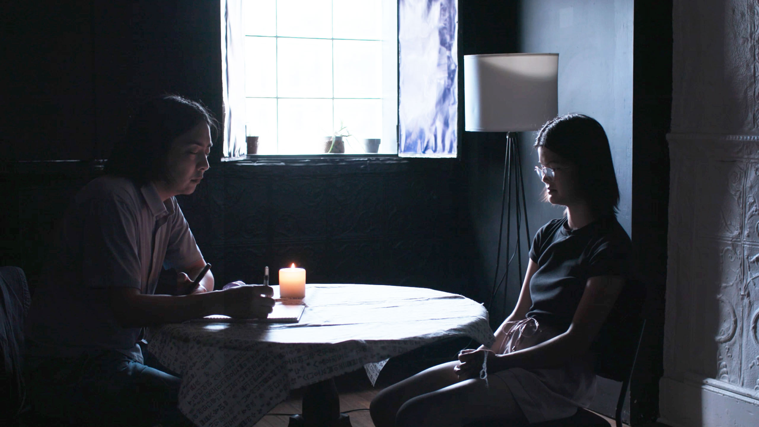 Two figures sit at a small round table, which has a candle on it.