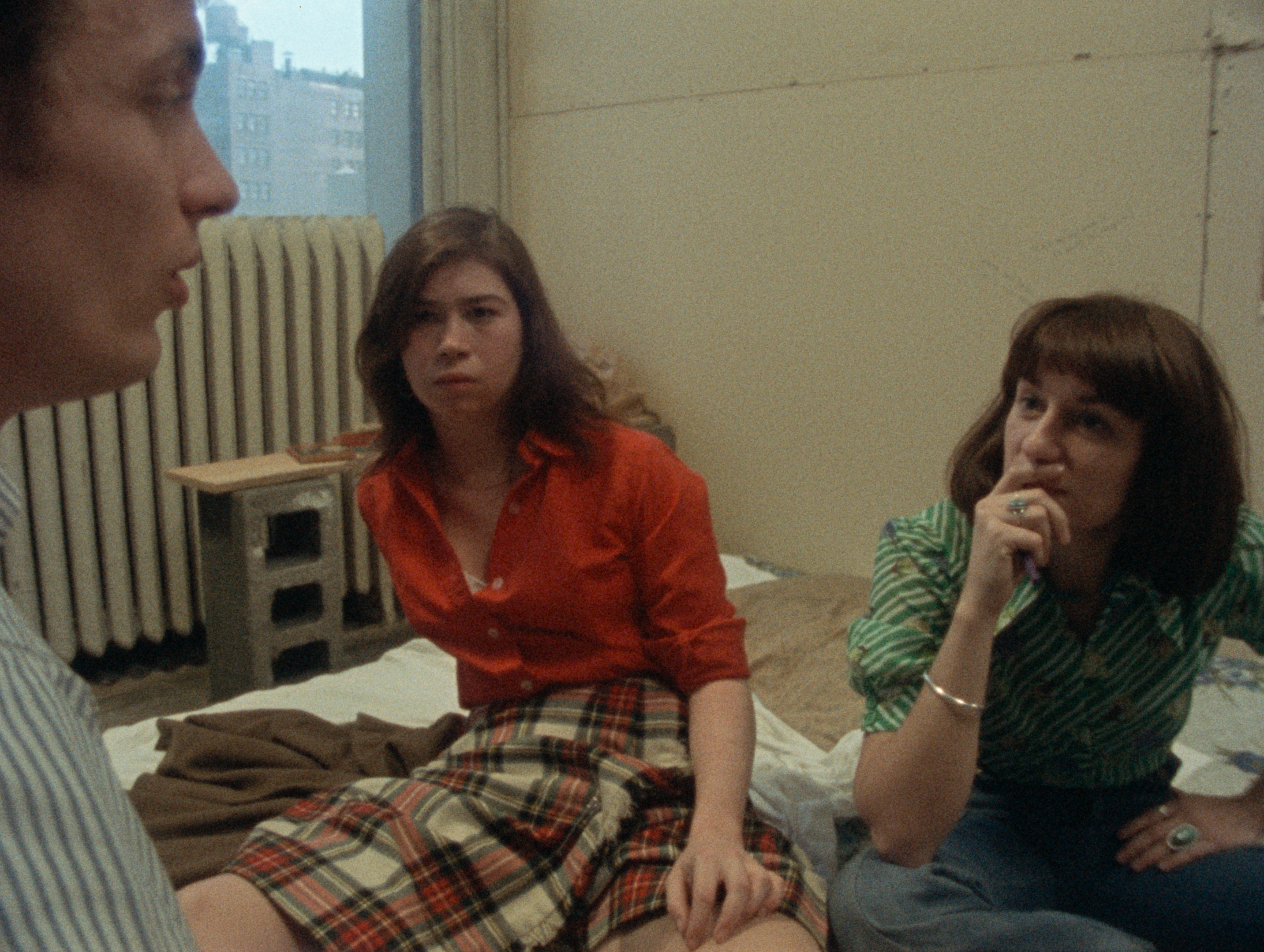 Three young people sit on a mattress on the ground.