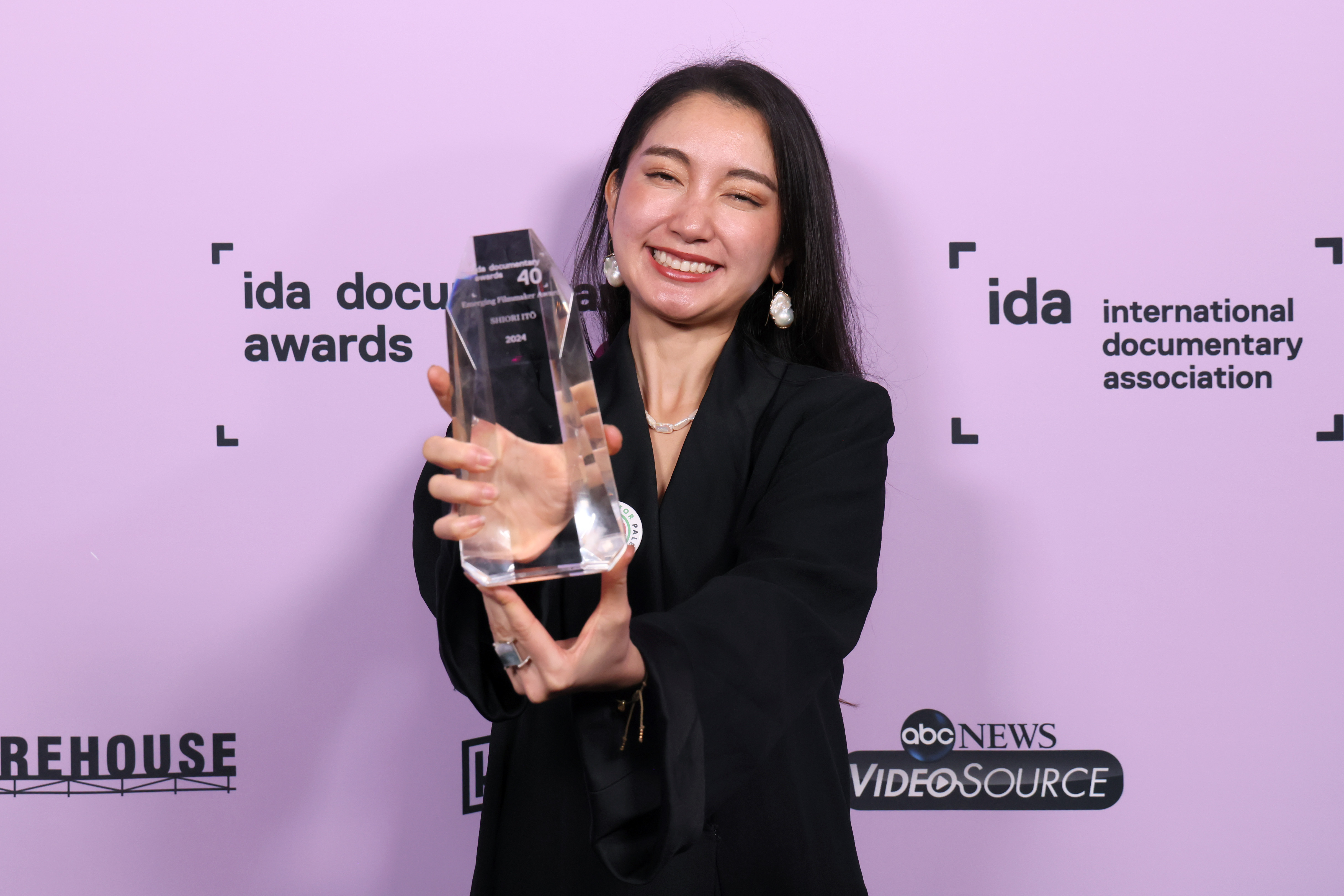 Shiori Ito, a woman with dark hair in a dark suit holding an IDA award close to the camera holds