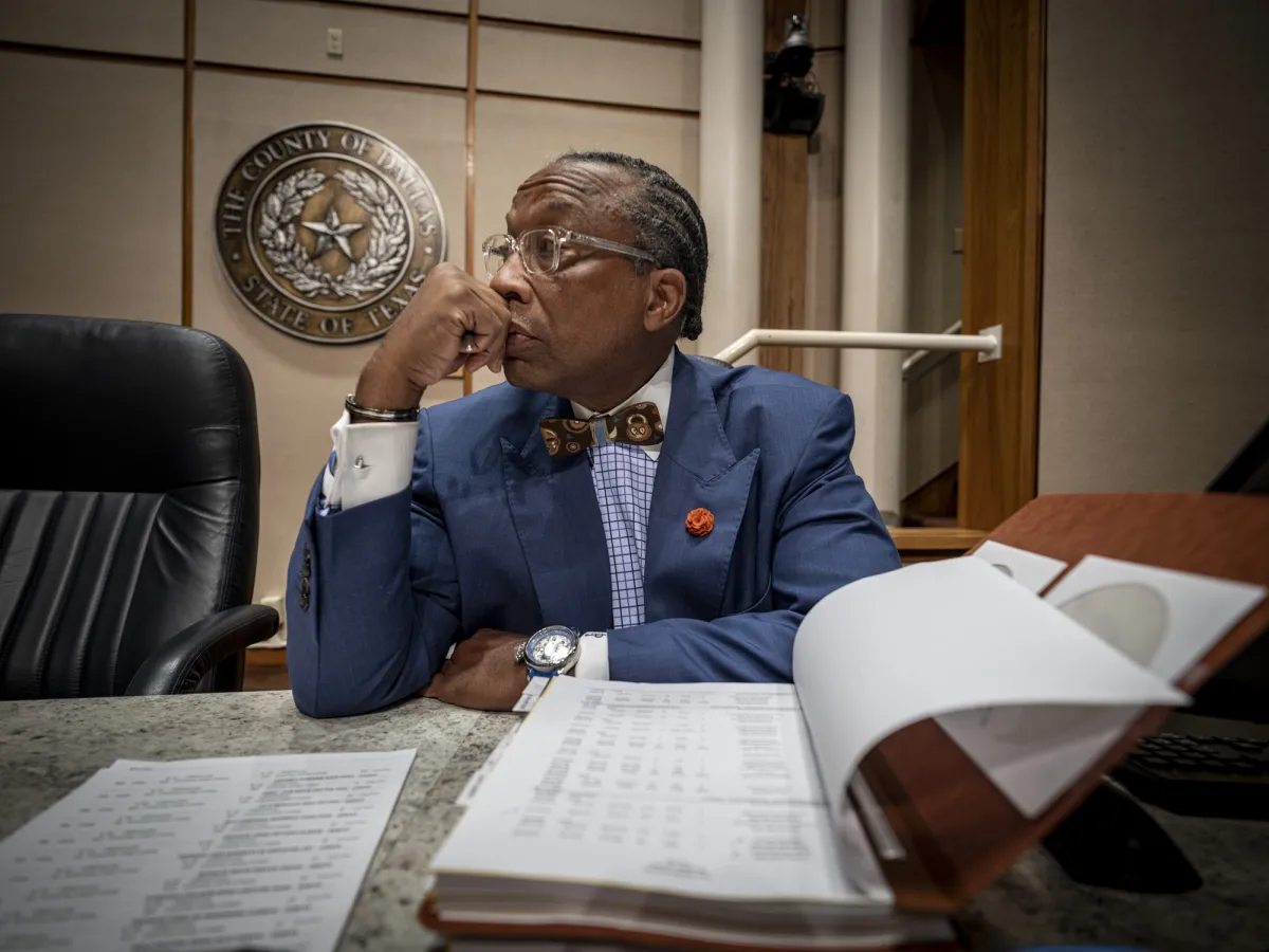 A Black man in a navy suit sits at a wooden courthouse table.