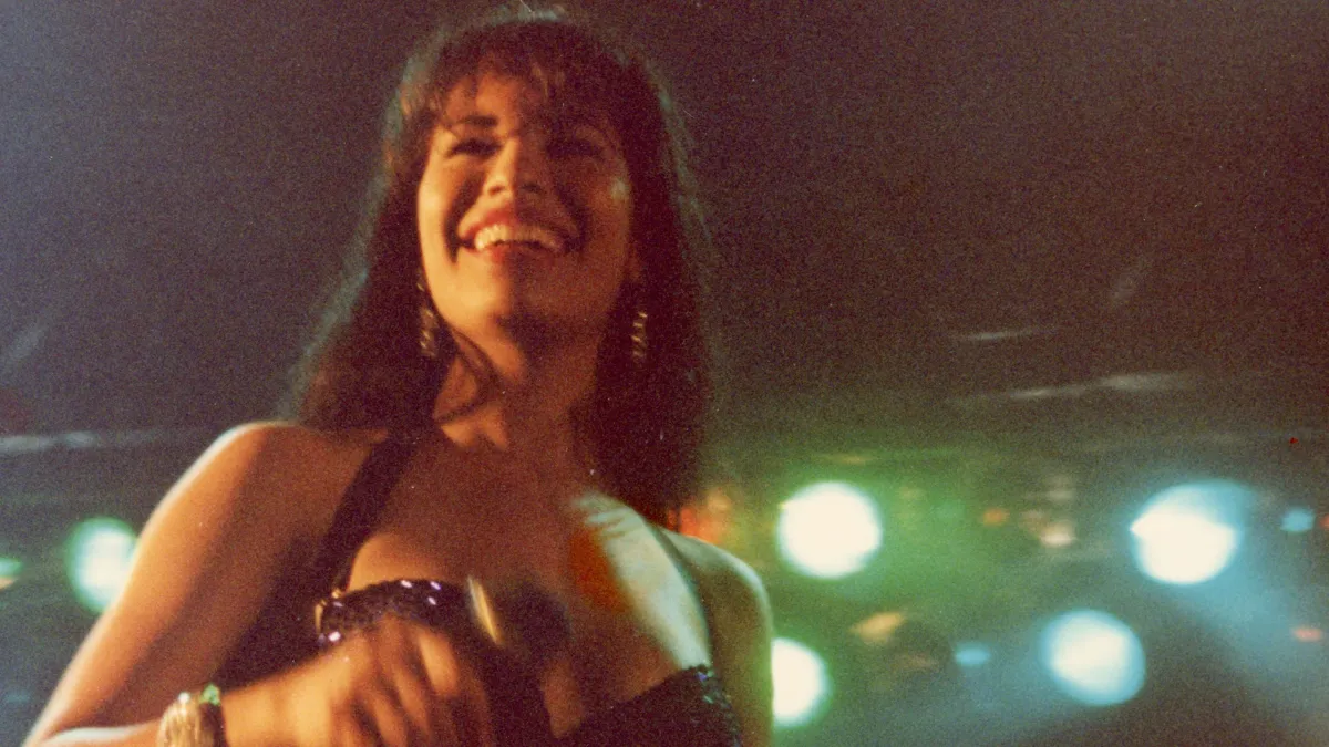 Grainy photograph of the singer Selena, standing in front of bright stage lights.