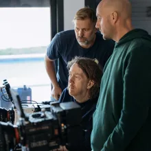 Three white men look at a camera monitor.